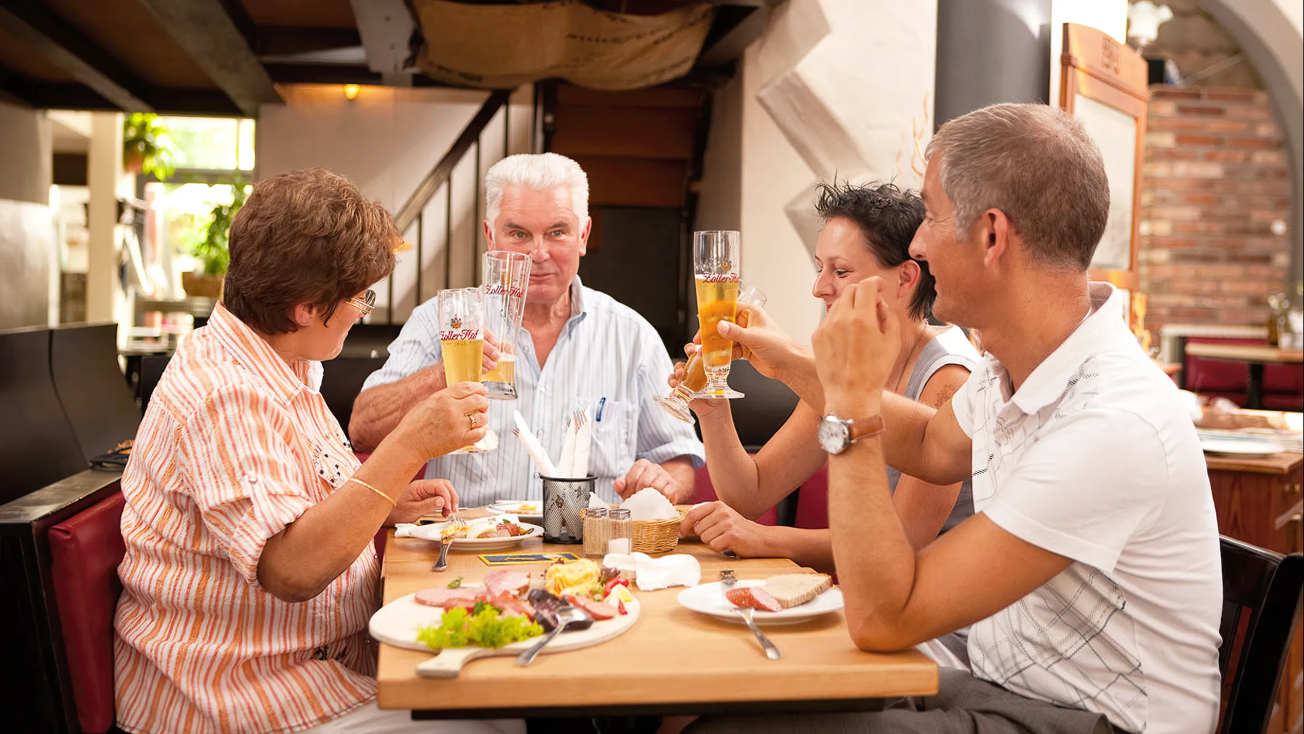 4 Personen sitzen an Tisch und essen und trinken Zoller-Hof Bier in Brauereigaststätte nach Brauereiführung